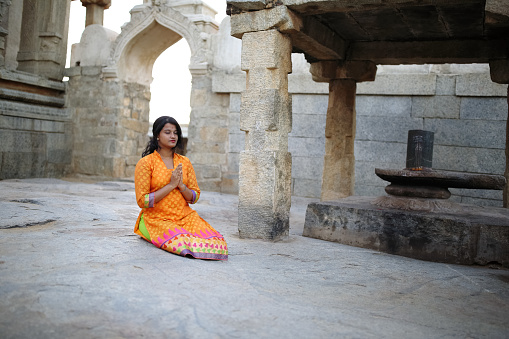 Young woman offering prayer sitting before the Shivalingam in the premises of an ancient temple at Lepakshi, Andhra Pradesh. The temple was built in 1538 CE and a popular tourist attraction in South India.