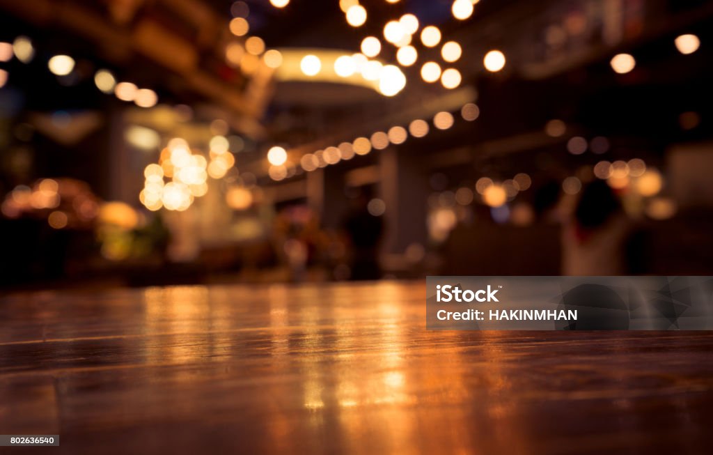 Wood table on blur cafe (bar) with light background Empty wood table top on blur cafe restaurant in dark background/selective focus .For montage product displayEmpty wood table top on blur cafe (restaurant) in dark night with light background/selective focus.For montage product display Bar Counter Stock Photo