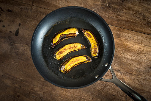 View of bananas fried on butter, and served on a hot nonstick cooking pan over a wooden table