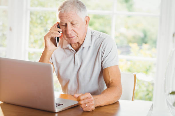 istock Concentrated senior man looking at laptop and phone calling 802649622