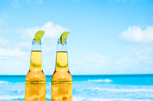 Two beer bottles with a slice of lime on a tropical beach.