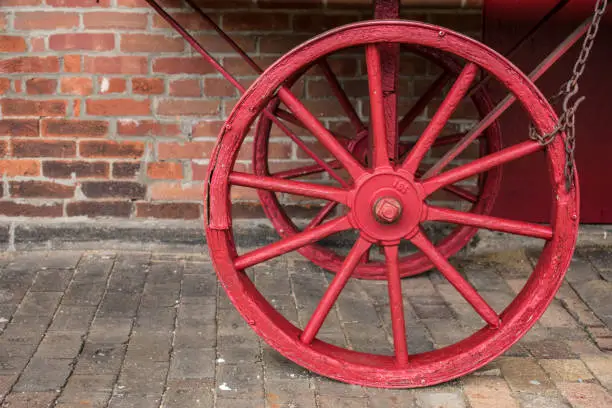 A red wagon wheel in front of a brick wall