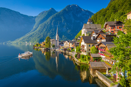 Scenic picture-postcard view of famous Hallstatt mountain village in the Austrian Alps with passenger ship in beautiful morning light on a sunny day in summer, Salzkammergut region, Austria