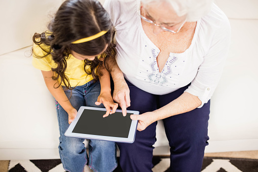 Concentrated granddaughter using tablet with grandmother at home