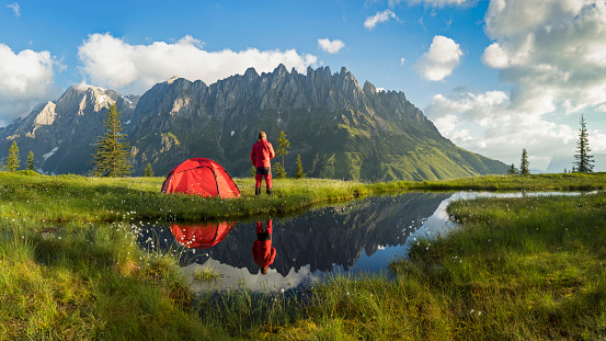 Camper in front of his tent with reflection in a pond at Hochkönig, Mandelwand