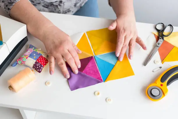 Photo of needlework and quilting in the workshop of a tailor woman on white background - tailor at work with pieces of colored cloth on the table with threads, fabrics, needles, sewing machine, rotary cutters