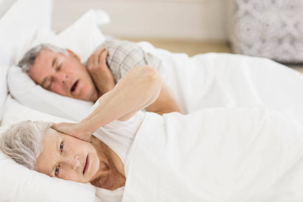 awake senior woman in bed covering her ears - quilt 60s 70s activity imagens e fotografias de stock