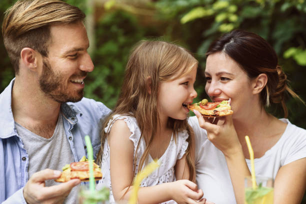 szczęśliwa rodzina jedząca pizzę na świeżym powietrzu - couple dinner summer sunlight zdjęcia i obrazy z banku zdjęć