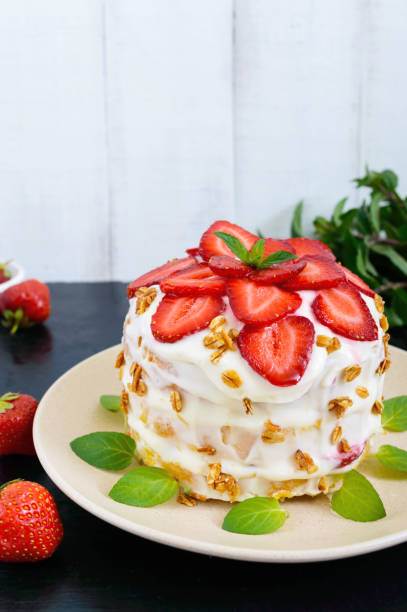 un gâteau de fête avec des fraises fraîches, crèmes, orné de feuilles de menthe sur fond noir. vue verticale - little cakes photos et images de collection