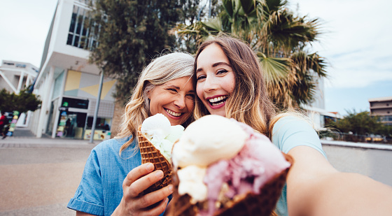 Beautiful middle-aged mother and adult daughter on summer holidays eating ice-cream and taking selfies