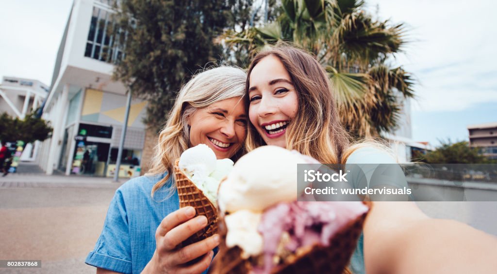 Senior mother and daughter taking a selfie while eating ice-cream Beautiful middle-aged mother and adult daughter on summer holidays eating ice-cream and taking selfies Ice Cream Stock Photo