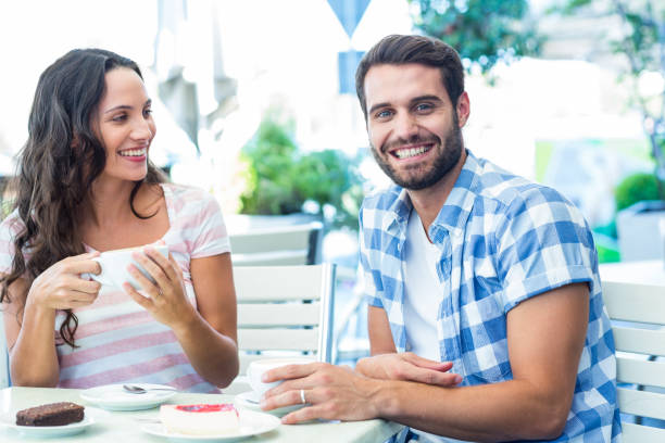 istock Cute couple sitting outside at a cafe with man smiling at camera 802857166