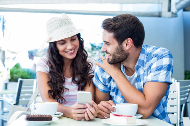 istock Cute couple sitting in cafe looking at smartphone 802857280