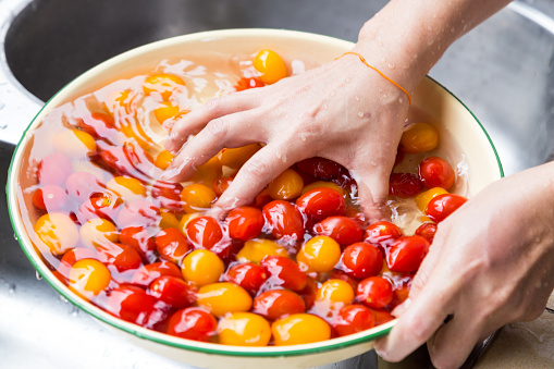 Hand washing cherry tomato with running water in household sink
