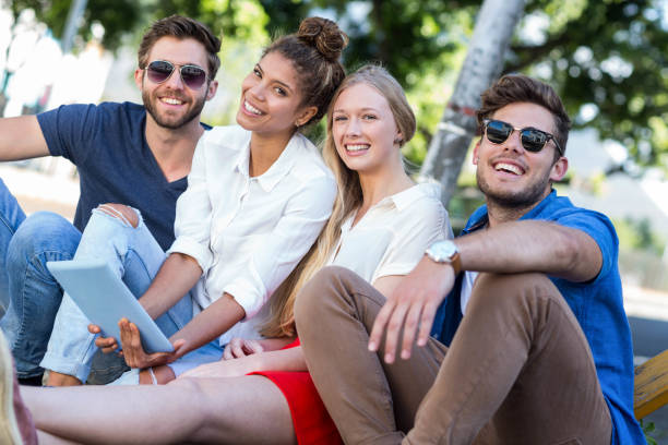 istock Hip friends holding tablet and sitting on sidewalk 802918082