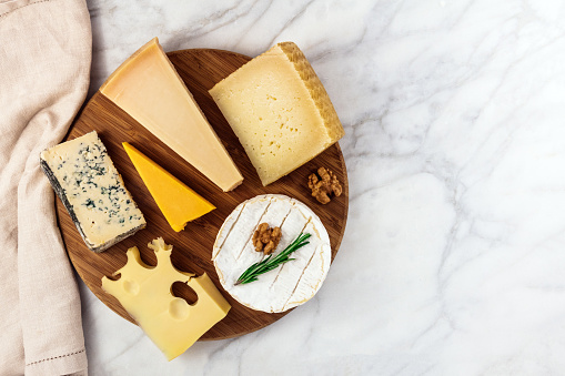An overhead photo of a selection of cheeses, shot from above on a white marble table, with a place for text