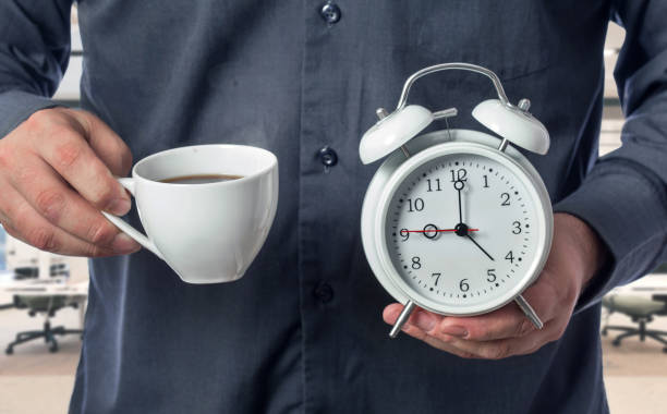 istock The office worker holds a cup of aromatic coffee and an alarm clock 802941776