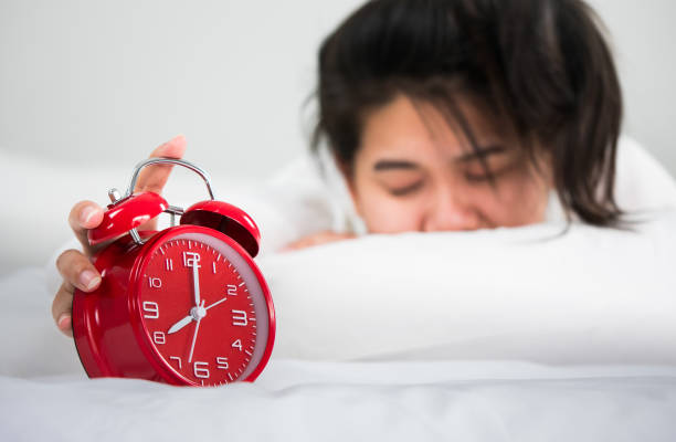 istock Asian women wake up from sleep. her hands hold at the clock 802944426