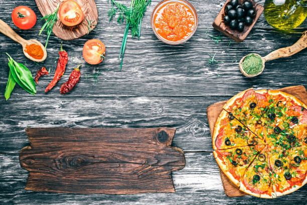 Pizza with ingredients Baked pizza and ingredients -fresh tomatoes, sauce, olive oil, green herbs and spices on background of black textured wood. Rustic signboard. Top view tarragon cutting board vegetable herb stock pictures, royalty-free photos & images