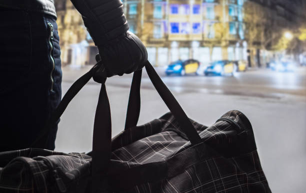 istock Terrorism and security threat concept. Terrorist at night. Suspicious man standing in city center holding black bag. Planning a bomb attack. Traffic, cars and buildings in the background. 802970330