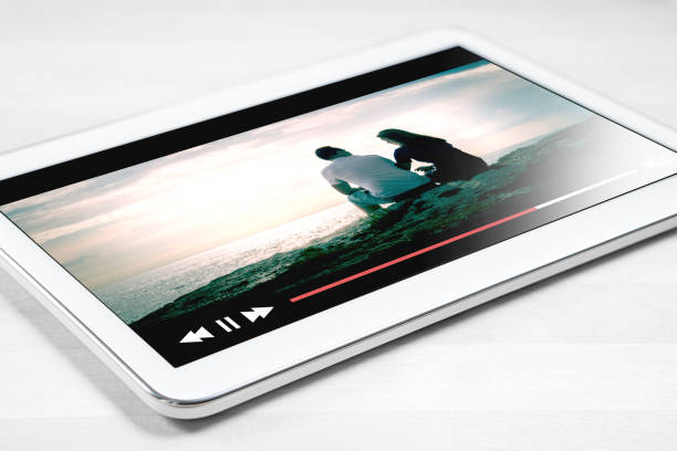 istock Online movie stream with mobile device. White tablet on wooden table with imaginary video player and film streaming service. 802970416