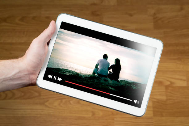 istock Man watching movie online with mobile device. Hand holding tablet with imaginary video player and film streaming service. 802970422