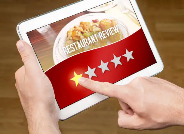 Photo of Bad restaurant review. Disappointed and dissatisfied customer giving terrible rating with tablet on an imaginary criticism site, application or website. One out of five stars to tavern, cafe or bistro