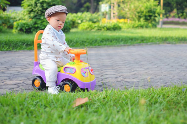 Cute little Asian 11 months old  baby boy child wearing bib and hat learning to ride his first running colorful bike in public park in spring time, stock photo