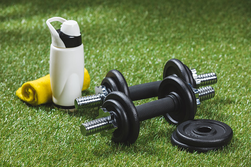 dumbbells with weight plates and bottle of water with towel on grass