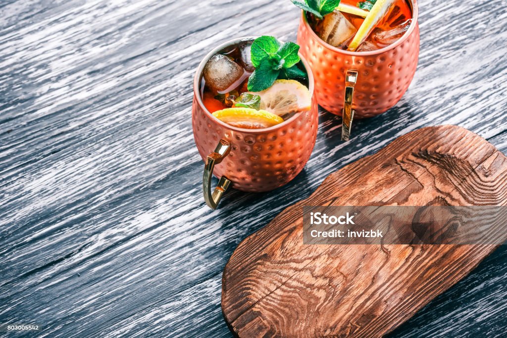 Mocscow mule cocktail with lemon Moscow mule cocktail with lemon and mint in copper mugs. Black wood background and brown wood tableware Moscow Mule Stock Photo