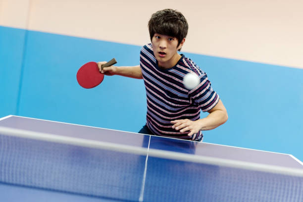 View of professional ping pong set with paddles resting on the net on green game table with white ball. Front view.