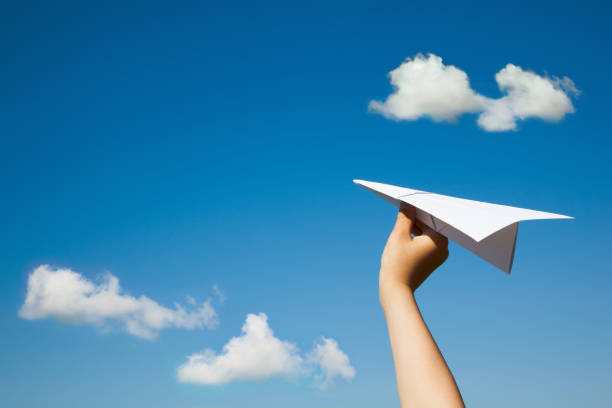 Paper plane in child hand. Paper plane in child hand on blue sky and clouds background. (With space for text.) paper airplane photos stock pictures, royalty-free photos & images