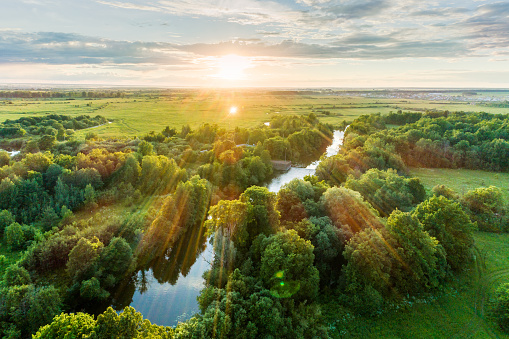 Landscape view from above. The countryside with a meadows, a groves and a winding river next to a town. Shooting at sunset in warm summer day