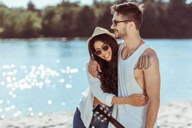 young smiling interracial couple in sunglasses embracing on riverside