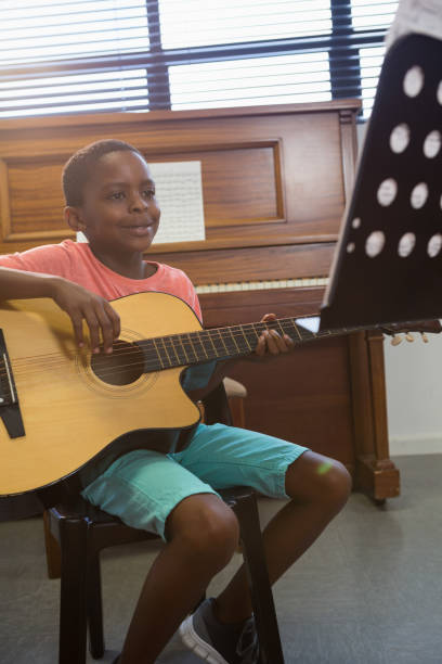 istock Happy boy playing guitar while sitting in classroom 803072240