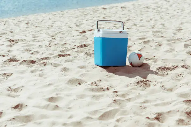 blue cooler box and volleyball ball on sandy beach