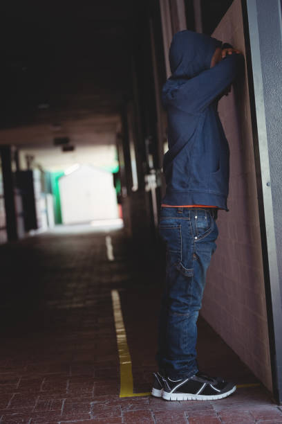 istock Side view of sad boy leaning on wall in corridor 803077590