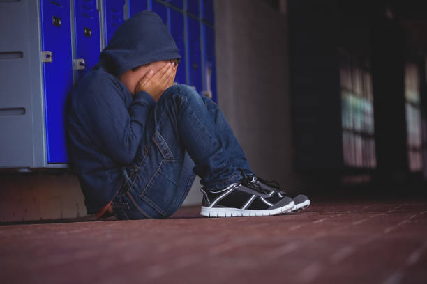 istock Boy sitting on pavement by lockers 803077734