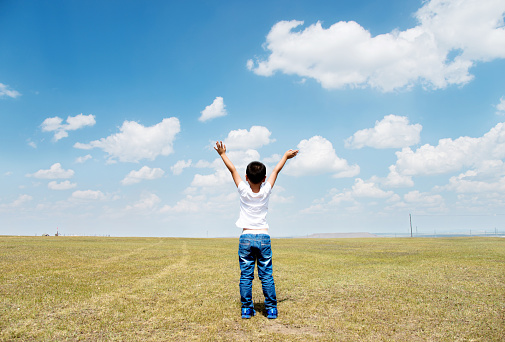 Little boy arms raised under blue sky