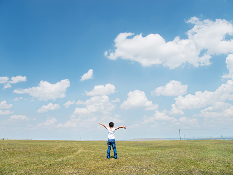 Little boy arms raised under blue sky