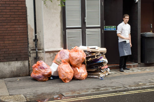 Garbage bags piled up outside of a restaurant awaiting collection. On the right is one of the chefs coming out of the restaurant doorway.