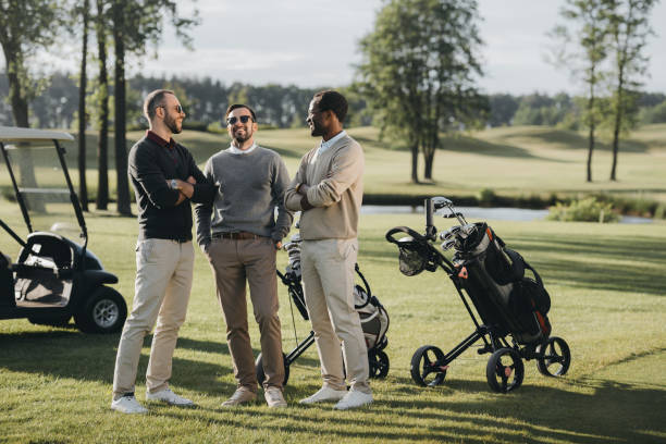 golfeurs multiethniques avec les clubs de golf parler et passer du temps ensemble sur le terrain de golf - golf cart golf mode of transport transportation photos et images de collection