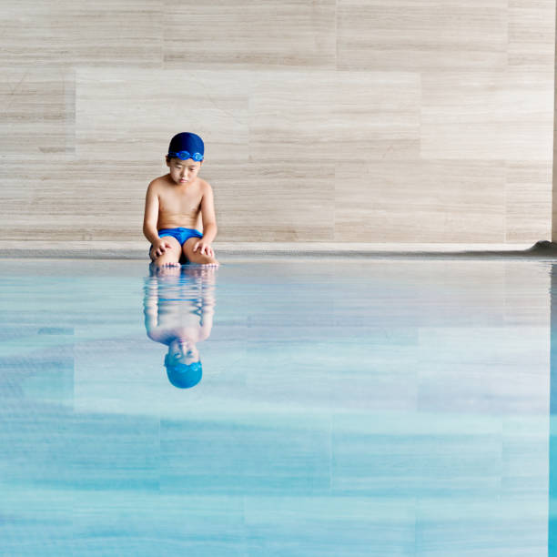 маленький мальчик, сидящий у бассейна - child swimming pool swimming little boys стоковые фото и изображения