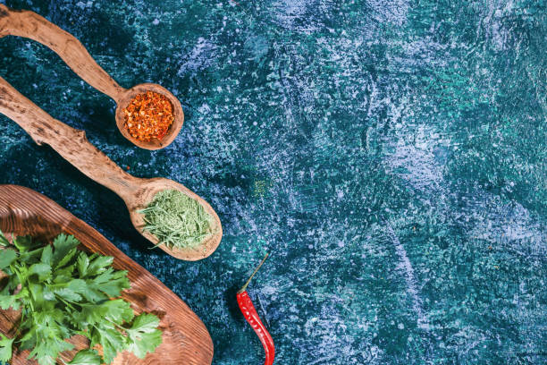 Fresh and dried herbs Fresh cilantro on wooden plate and dried spices in wooden spoons over dark blue spotty background. Top view tarragon cutting board vegetable herb stock pictures, royalty-free photos & images