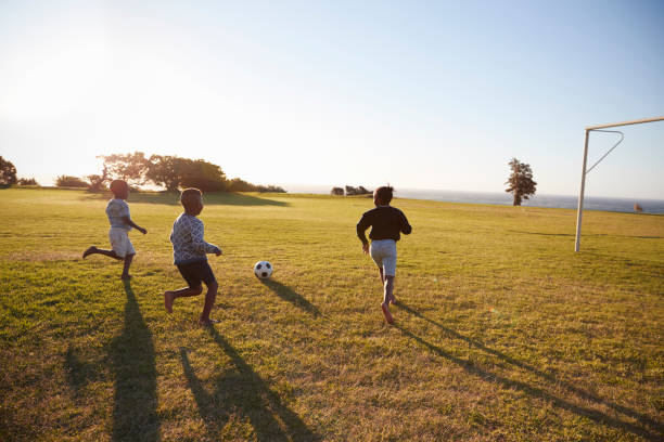 istock Three elementary school kids playing football in a field 803138200