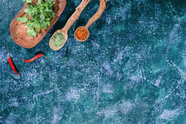 Fresh and dried herbs Fresh cilantro on wooden plate and dried spices in wooden spoons over dark blue spotty background. Top view tarragon cutting board vegetable herb stock pictures, royalty-free photos & images