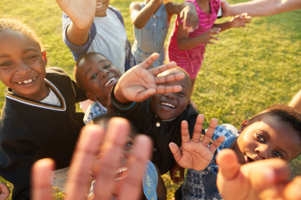 istock Elementary school kids in a field look up at  camera waving 803138438