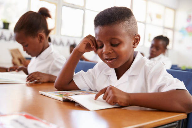 istock Elementary school boy reading a book at his desk in class 803145374