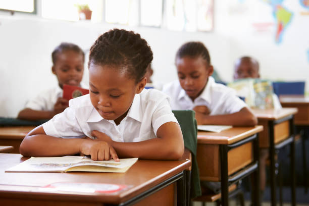 menina lendo na mesa na aula de ensino fundamental - africa child reading african descent - fotografias e filmes do acervo