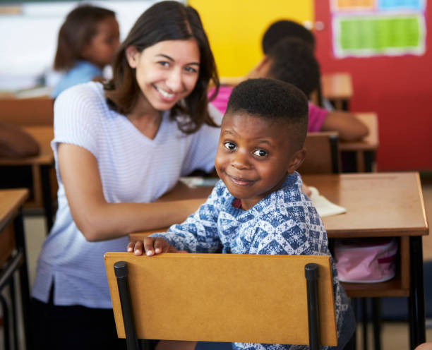 カメラに微笑む女性のボランティア教師と小学生の少年 - elementary school waist up indoors childhood ストックフォトと画像